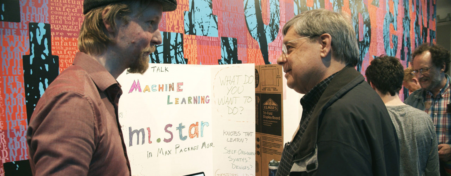 A presenter at a music technology fair explains his project to someone attending.