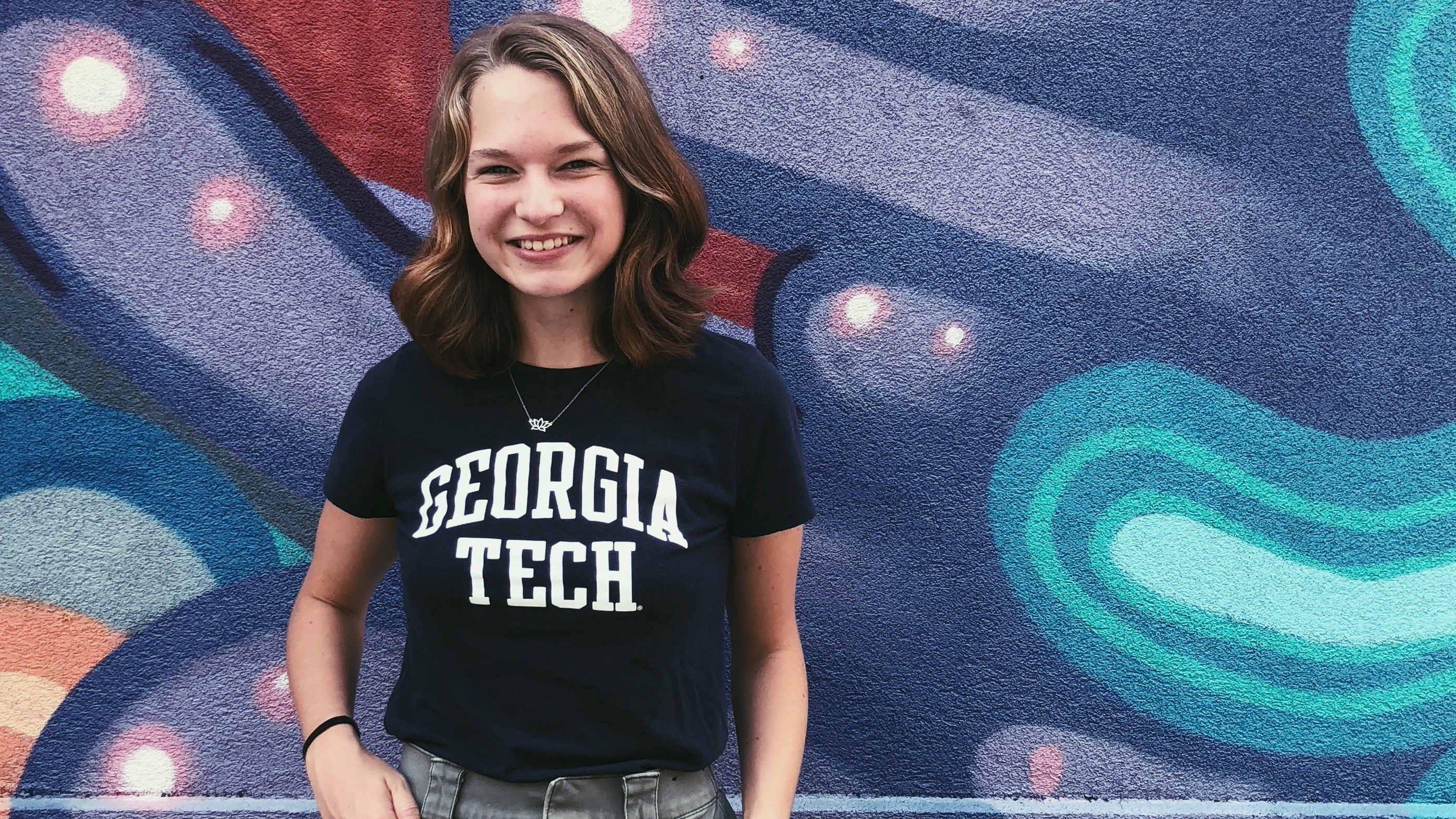 Ally Stout wearing a Georgia Tech shirt and posing in front of wall art in tones of blue and purple.