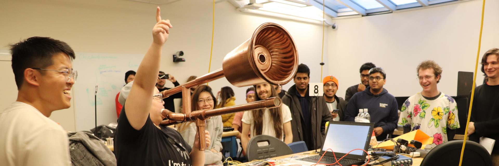 A Moog Hackathon finaliist playing a modified trombone to a crowd of competitors.