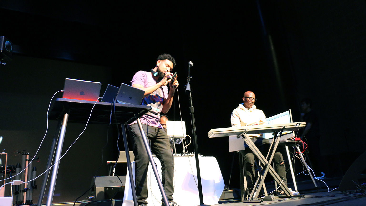 Two men performing on stage, using a phone and a computer.