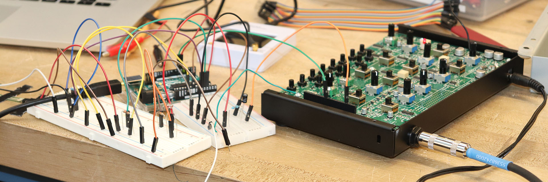 A Moog Synthesizer opened to reveal the parts inside, sitting next to a circuit board on a work table.