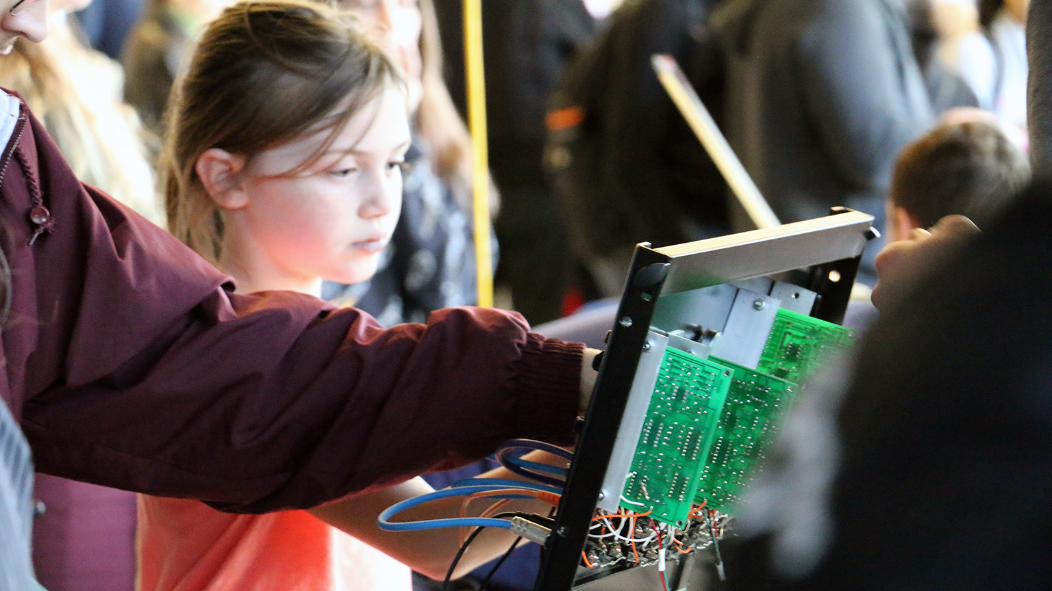 A girl reaching out to touch a panel with circuitry attached to it.
