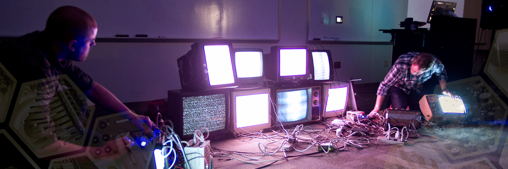 Two people on either side of a stack of cathode ray tube TVs showing static on the screens.